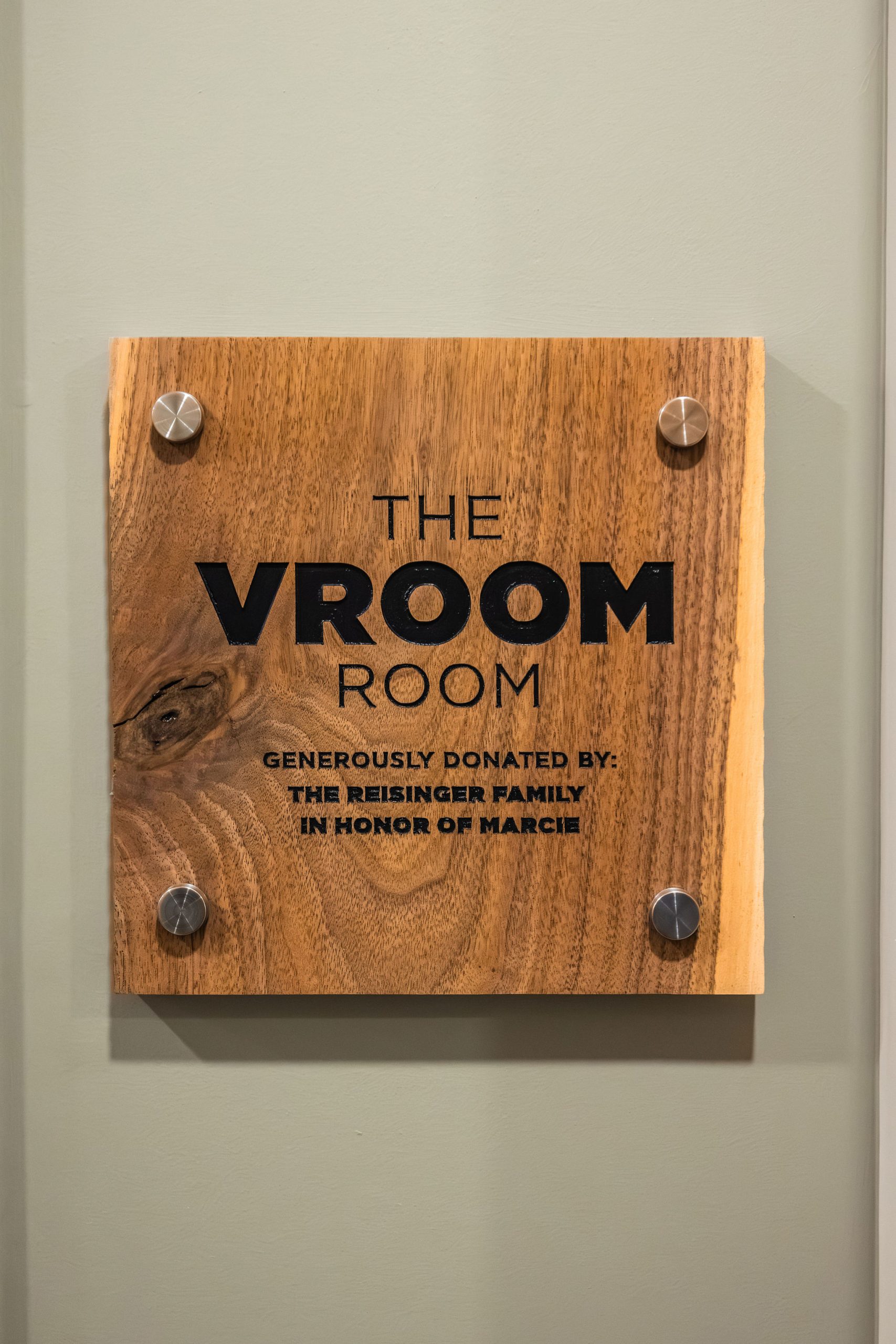 Wood sign with The Vroom Room generously donated by The Reisinger family in honor of Marcie written on it.